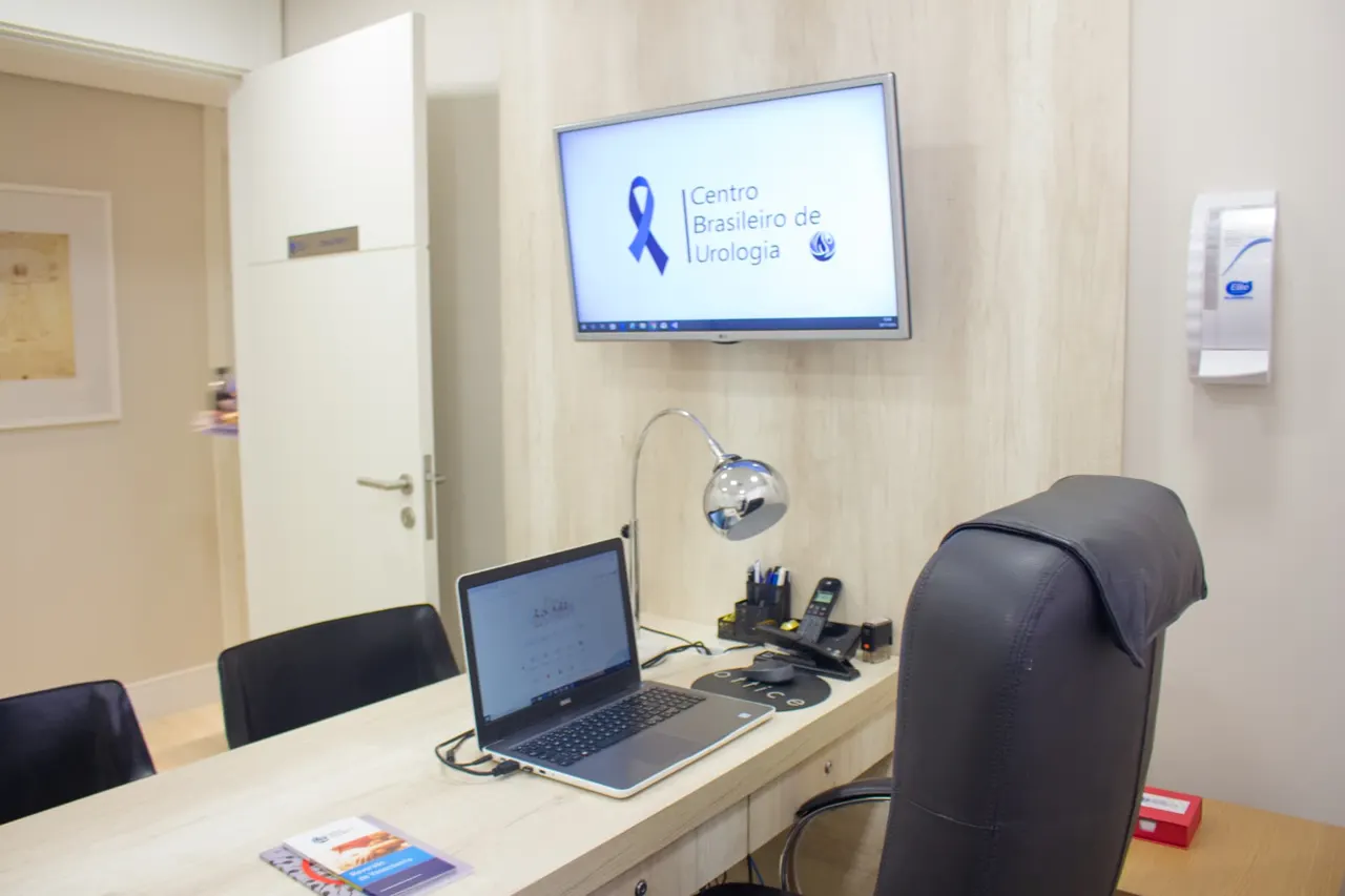 Consultório com mesa, notebook e televisor com a marca do Centro Brasileiro de Urologia