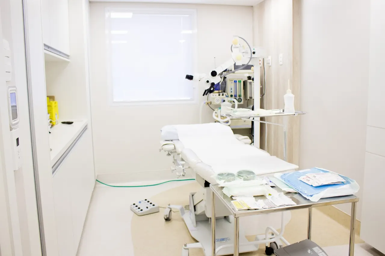 Sala de procedimentos com mesa cirúrgica, microscópio e materiais estéreis