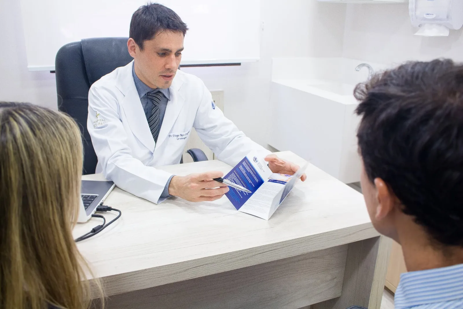 Dr. Diego Reis Delgado explicando orientações em consulta com um casal, usando um folheto