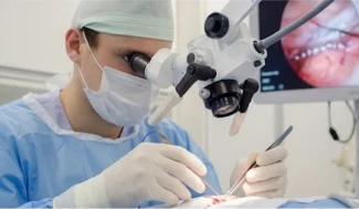 Cirurgião operando com microscópio cirúrgico em procedimento de microcirurgia